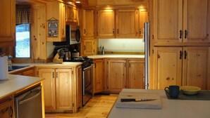 A kitchen with wooden cabinets, a refrigerator, a stove, and a window with a view. - AMAZING WATERFRONT SUNSETS ! (Ossipee)
