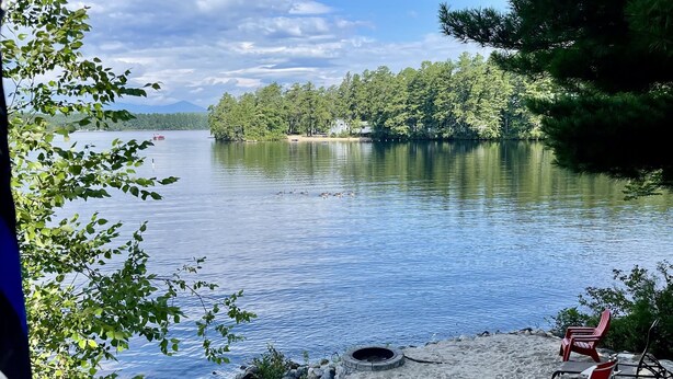A lakeside view with a deck, red chairs, and a fire pit. - AMAZING WATERFRONT SUNSETS ! (Ossipee)