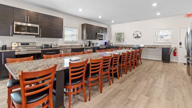 A modern kitchen with dark wood cabinets, stainless steel appliances, a granite countertop island, and a long dining table with wooden chairs. - PERFECT GETAWAY Home Private POOL+SPA Poker+Pool Table, GREAT LOCATION! (North Myrtle Beach)