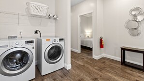 A laundry room with two front-loading washing machines, a white laundry basket on a shelf, a fire extinguisher, and a wooden bench. - PERFECT GETAWAY Home Private POOL+SPA Poker+Pool Table, GREAT LOCATION! (North Myrtle Beach)