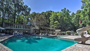 A swimming pool with lounge chairs and a slide, surrounded by trees and a building with a covered patio.