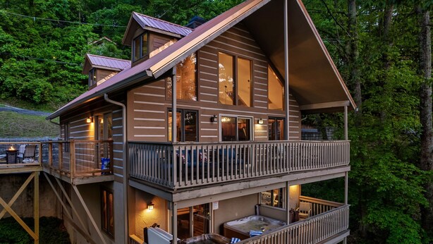 A two-story log cabin with a balcony, outdoor seating, and a hot tub.
