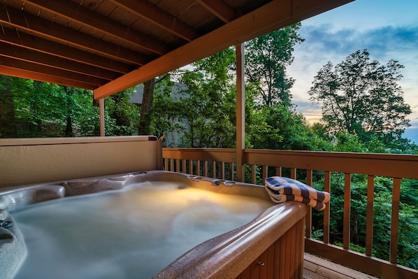 Ein Whirlpool auf einer Holzterrasse mit Blick auf Bäume und ein Haus im Hintergrund.