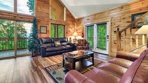 A spacious living room with wooden walls, a leather sofa, a coffee table, and a staircase.