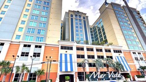 A hotel with multiple high-rise buildings, a prominent entrance with a blue and white striped awning, and palm trees in the foreground.