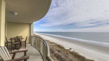 A balcony with a view of the beach, a table with chairs, and a railing.