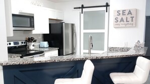 Una cocina moderna con una isla azul oscuro, electrodomésticos de acero inoxidable, taburetes blancos y un letrero que dice 'Sea Salt cures everything'.