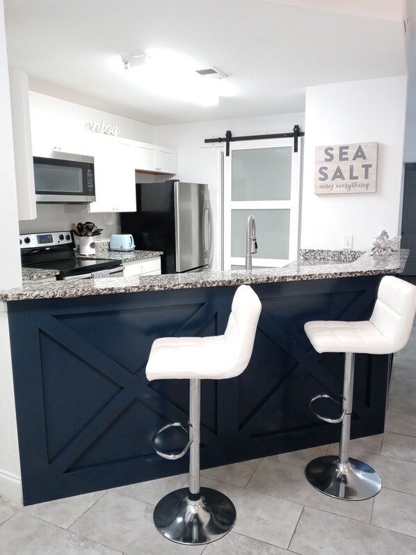 A modern kitchen with a dark blue island, stainless steel appliances, white bar stools, and a 'Sea Salt cures everything' sign.