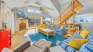 A spacious living room with a high ceiling, a fireplace, a large window with a view, a staircase, and a cozy seating area. - Oceanfront Dog Friendly Home w/ Hot Tub, Foosball, and Direct Beach Access (Avon)