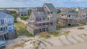 A beachfront property with multiple levels, including a prominent upper deck with outdoor seating. - Oceanfront Dog Friendly Home w/ Hot Tub, Foosball, and Direct Beach Access (Avon)