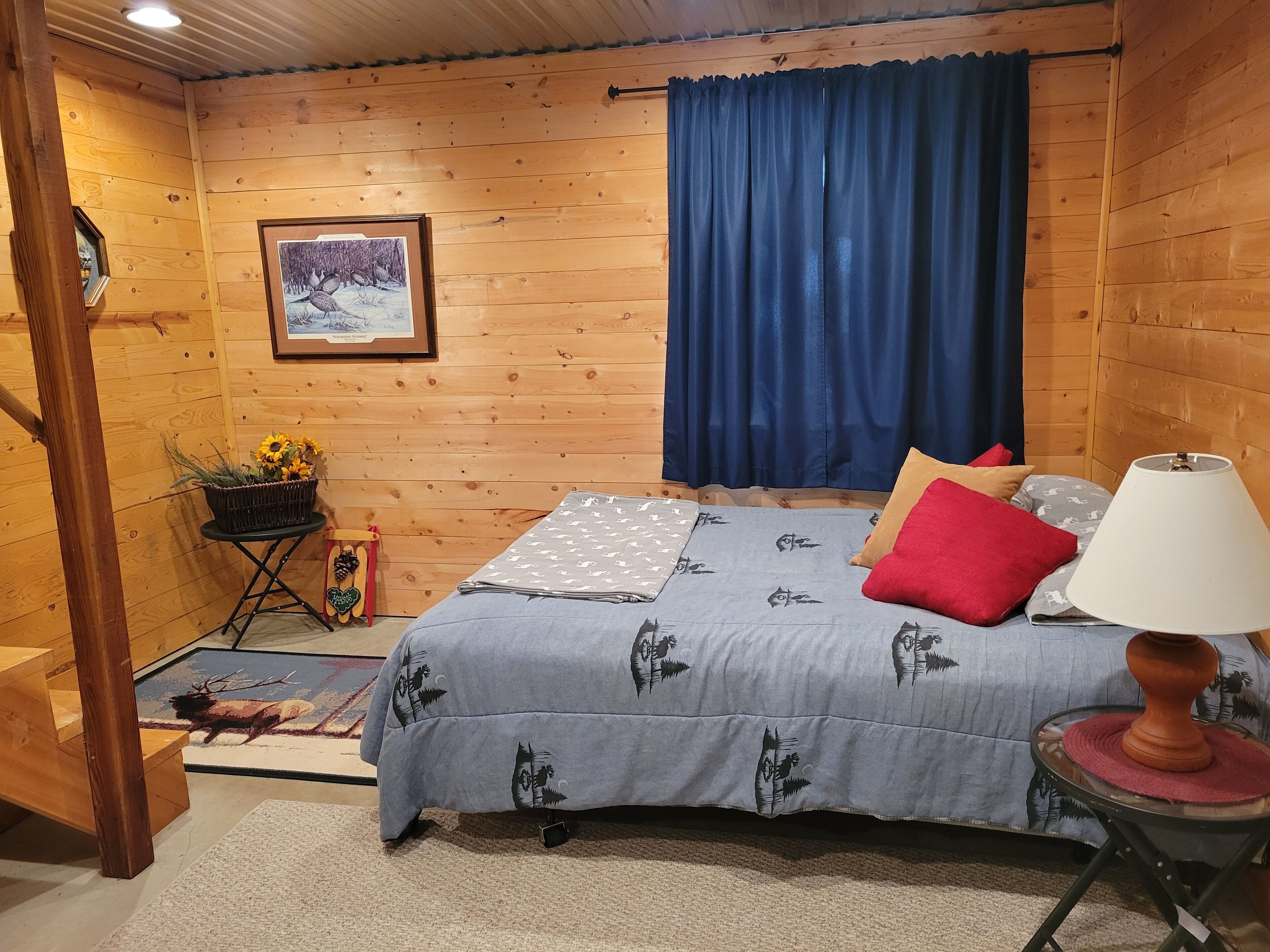 A cozy wooden cabin room with a bed, a lamp, and a framed picture on the wall.