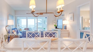 A bright, airy dining room with a white table and chairs, a chandelier, and a view of the ocean through large windows. - Direct Gulf Front ! Completely Renovated Modern 2 Bedroom ! (Sanibel)
