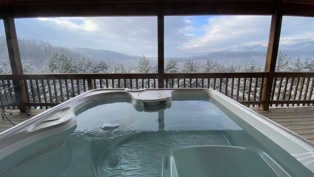 Un jacuzzi en una terraza de madera con vistas a montañas nevadas.