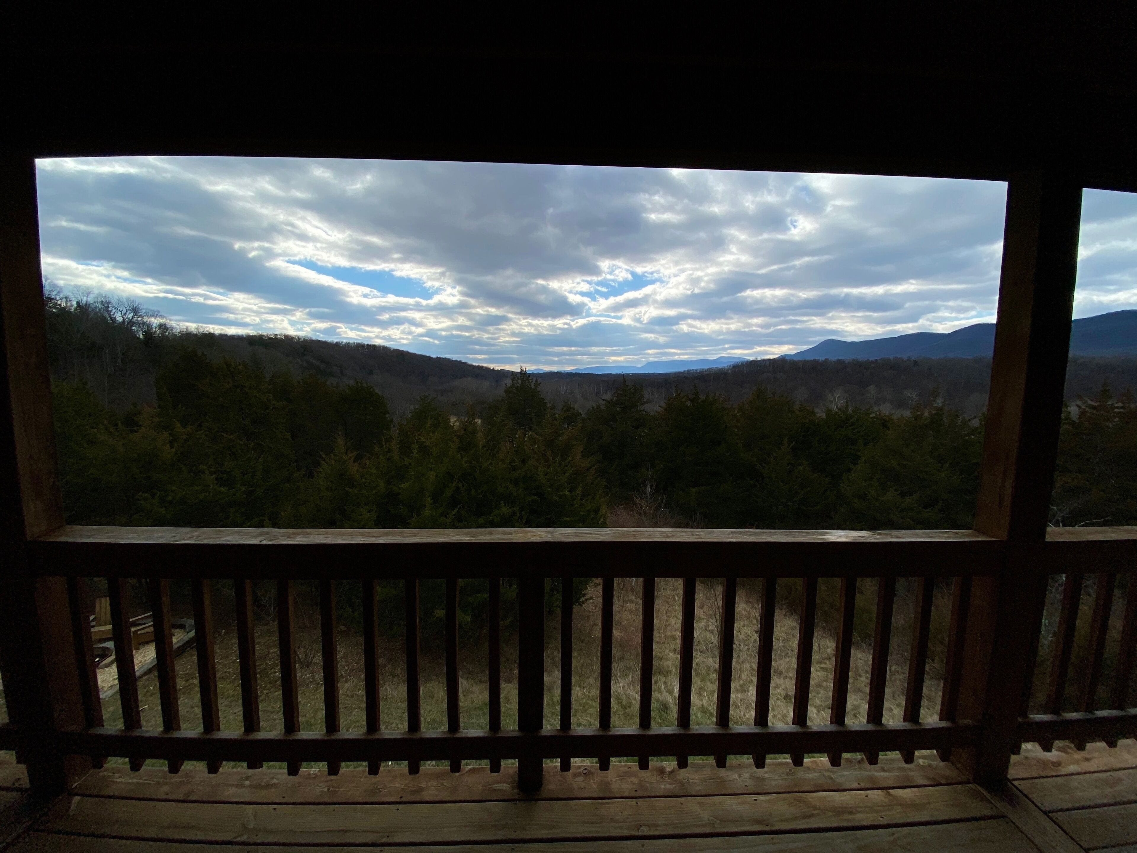 Ein hölzerner Balkon mit Blick auf eine bewaldete Landschaft und Berge unter einem bewölkten Himmel.