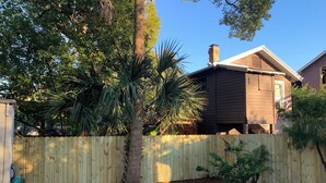 Ein Garten mit Holzzaun, gepflasterter Terrasse und einem Haus im Hintergrund.