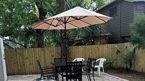 Ein Hinterhof mit einer Terrasse, einem Grill, Gartenmöbeln und einem Holzzaun.
