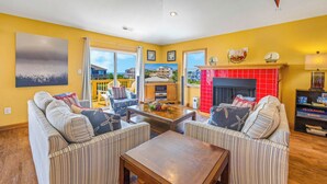 A living room with striped sofas, a wooden coffee table, a fireplace, and a balcony with a view. - Soundside Dog Friendly Home w/ Pool, Hot Tub, Game Room, Community Boat Ramp (Salvo)