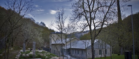 A modern building with a stone facade, surrounded by a landscaped garden with large rocks and trees.