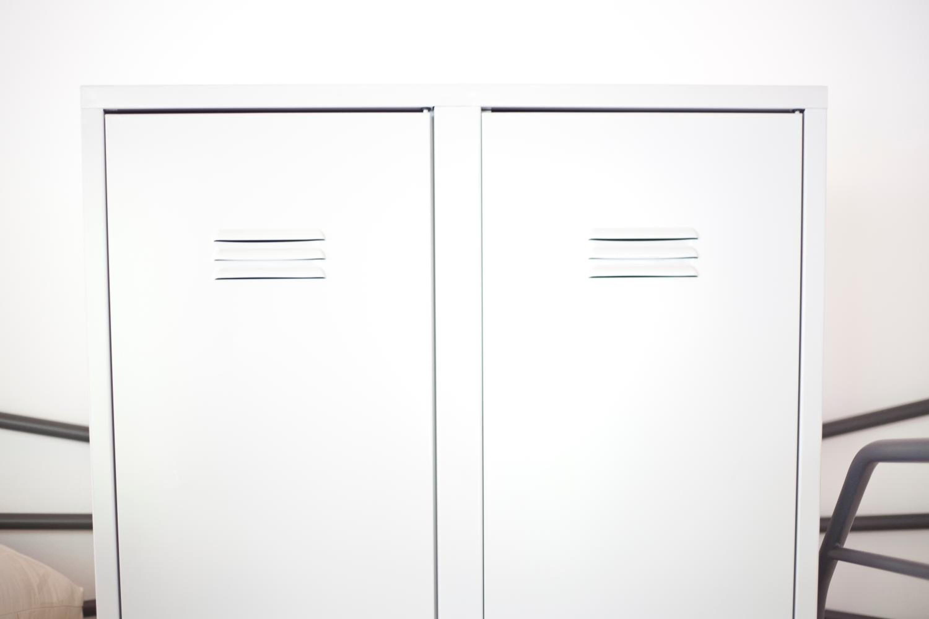 Dos taquillas metálicas blancas con líneas horizontales, probablemente para identificación, sobre un fondo uniforme.
