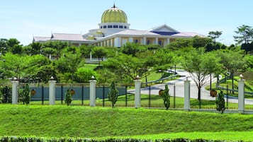 A large, historic building with a prominent dome and multiple smaller domes, surrounded by lush greenery and a well-maintained fence.