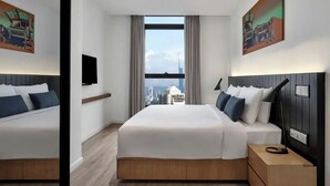 A modern hotel room with a large bed, a bedside table, a TV, and a city view through the window.