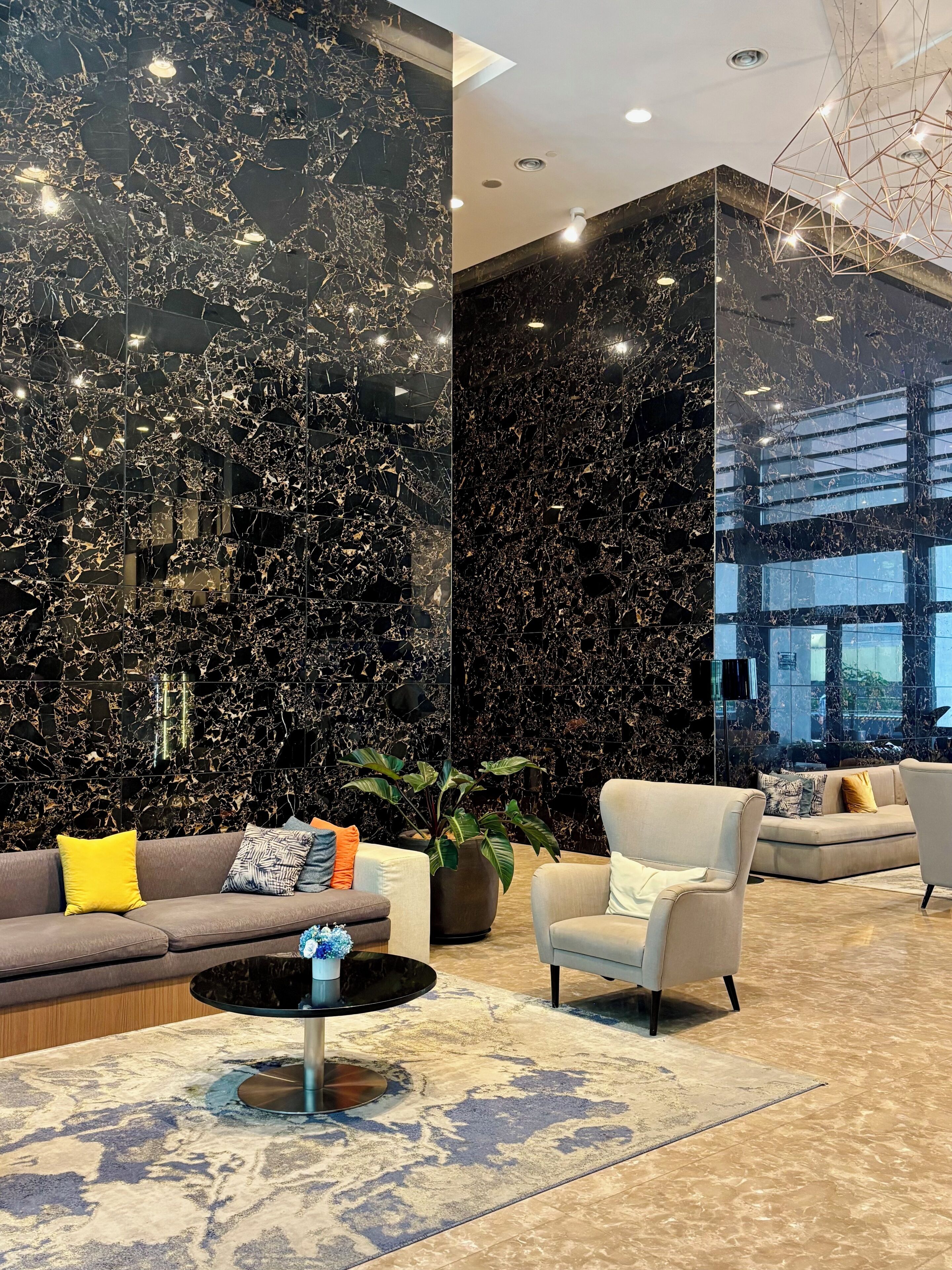 A modern lobby with a marble wall, a sofa with cushions, a round coffee table, and a potted plant.