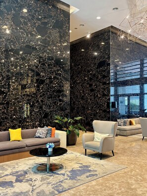 A modern lobby with a marble wall, a sofa with cushions, a round coffee table, and a potted plant. - Hyatt House Kuala Lumpur, Mont Kiara (Kuala Lumpur)