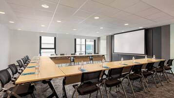 A conference room with a long table, chairs, a projector screen, and a carpeted floor.