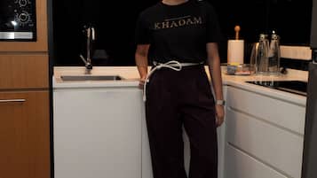 A person standing in a modern kitchen with wooden cabinets, a black countertop, and a stainless steel range hood.