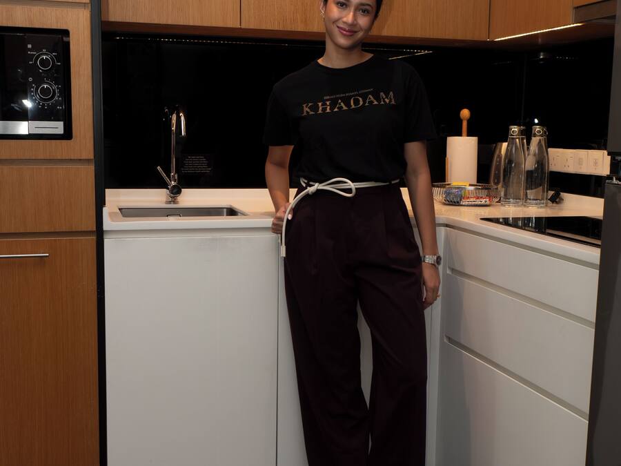 A person standing in a modern kitchen with wooden cabinets, a black countertop, and a stainless steel range hood.