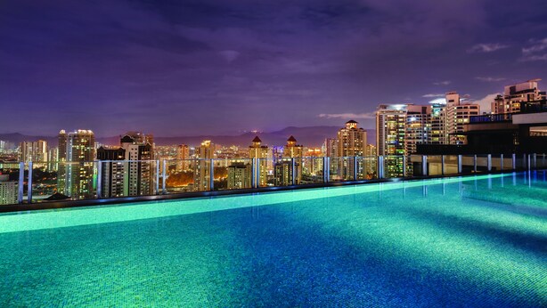 A rooftop infinity pool with a city skyline view at night.