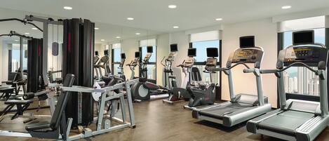 A modern gym with various exercise equipment, large windows, and a clean, well-lit interior.