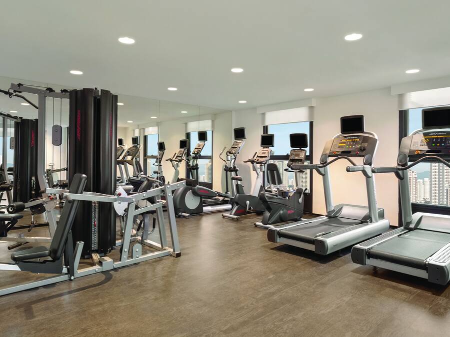 Un gimnasio moderno con diverso equipo de ejercicio, amplias ventanas y un interior limpio y bien iluminado.