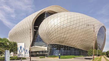 A modern architectural building with a unique curved design, large glass windows, and a well-maintained surrounding area with greenery and clear skies.