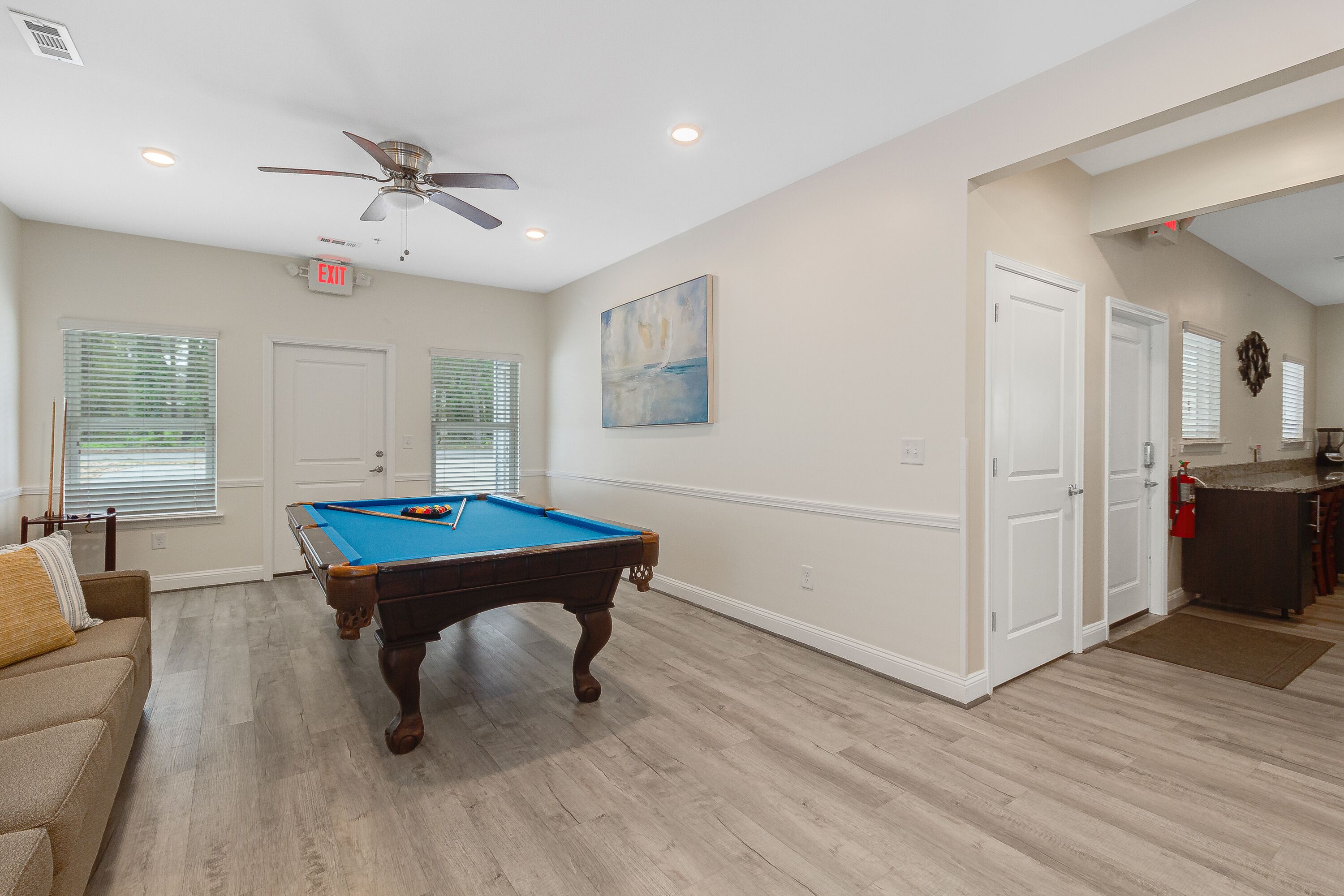 Une salle de jeux avec une table de billard, un ventilateur de plafond et un tableau accroché au mur.