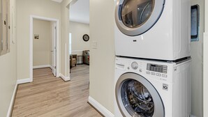 A laundry room with stacked washers and dryers, a wooden floor, and a hallway leading to a living area. - GREAT FOR GROUPS! LUXURY PRIVATE POOL+SPA, GATHERING SPACES, AMAZING LOCATION (North Myrtle Beach)