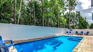 A swimming pool with blue water, surrounded by a white fence and trees. There are blue chairs and a small table near the pool. - GREAT FOR GROUPS! LUXURY PRIVATE POOL+SPA, GATHERING SPACES, AMAZING LOCATION (North Myrtle Beach)