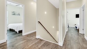 A spacious room with a wooden floor, a bed, and a staircase with a glass railing. - GREAT FOR GROUPS! LUXURY PRIVATE POOL+SPA, GATHERING SPACES, AMAZING LOCATION (North Myrtle Beach)