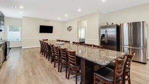A spacious kitchen with a granite countertop, stainless steel appliances, and a dining area with wooden chairs and a large table. - GREAT FOR GROUPS! LUXURY PRIVATE POOL+SPA, GATHERING SPACES, AMAZING LOCATION (North Myrtle Beach)