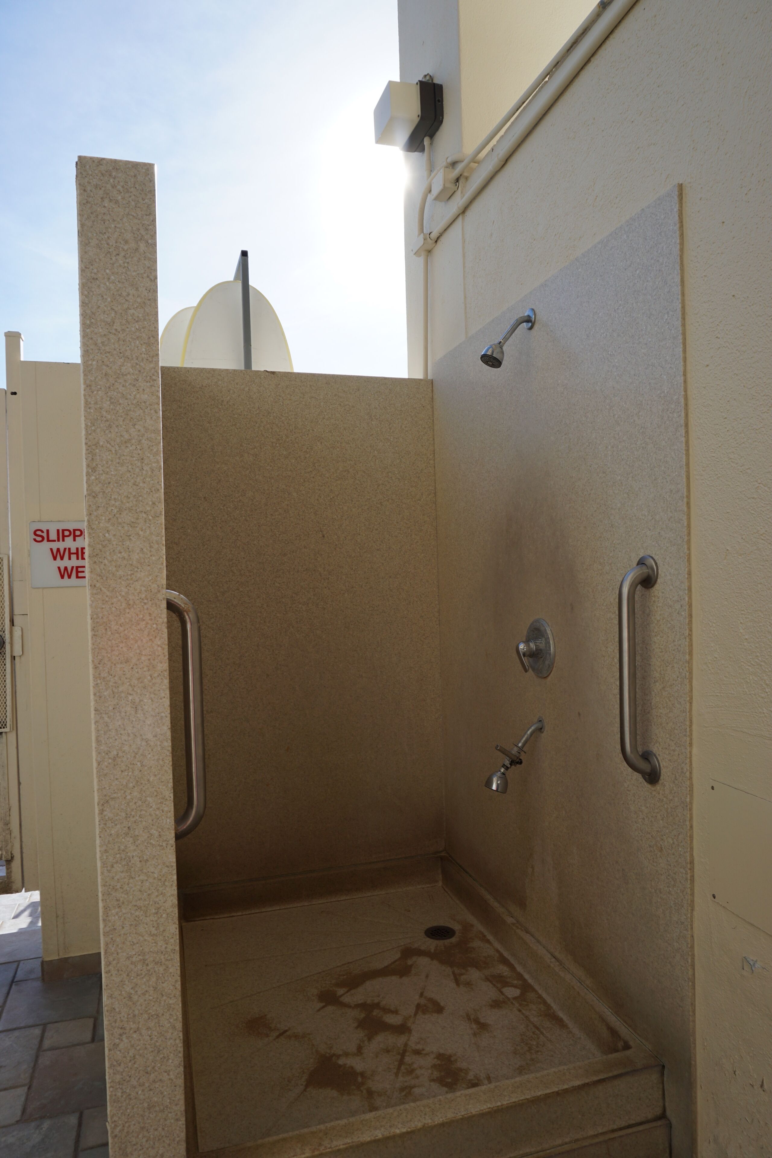 A shower stall with a sign that reads "SLIP WHILE WE".