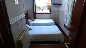 A narrow corridor with two single beds, a radiator, and a window with a view of the outside. - Pensión Santa María (Portugalete)