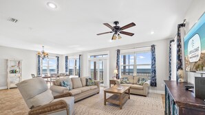 A spacious living room with a large window, a ceiling fan, and a view of the ocean.