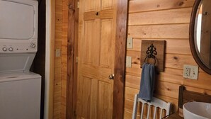 A wooden interior with a washing machine, a door, a chair, and a sink. - Cottage on the Kennebec (Caratunk)