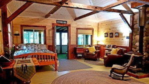 A cozy cabin interior with a bed, a fireplace, a rocking chair, and a stone wall. - Cottage on the Kennebec (Caratunk)