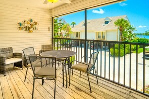 A balcony with a round table and chairs, a wicker sofa, and a view of a house and palm trees. - Two Free Kayaks included ! (Captiva)