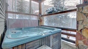 Un jacuzzi en una cabaña de madera con paredes de piedra y vistas a árboles nevados.