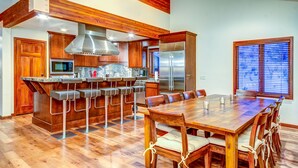 Una cocina amplia con una isla central, taburetes de bar y un comedor con una gran mesa de madera y sillas.