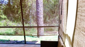 Moderni ulkotila, jossa on pehmustettu penkki ja lasipöytä, ja josta avautuu näkymä metsäiselle alueelle.