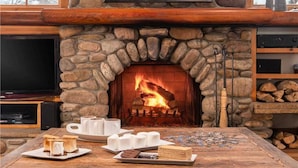 Une cheminée en pierre avec un feu, une table en bois avec de la nourriture et des boissons, et un téléviseur sur le côté gauche.