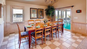 Un coin repas avec une table et des chaises en bois, un lustre et une vue à travers une porte vitrée.